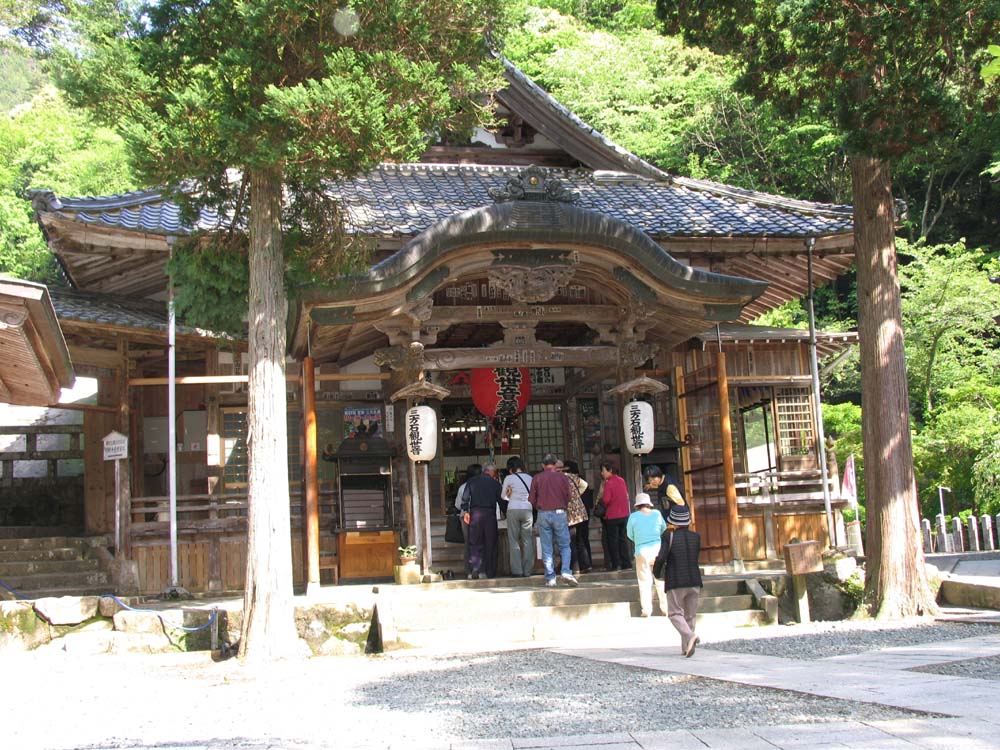 木でできた瓦屋根の本堂の真ん中に赤の大きい提灯とその両脇に白い提灯がありお賽銭に来た人たちが並んでいる三方石観世音の写真