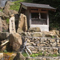 石積みの壁のようなものの上に小屋のようなものが建っており手前に観音霊水と書かれた石碑が建っている写真