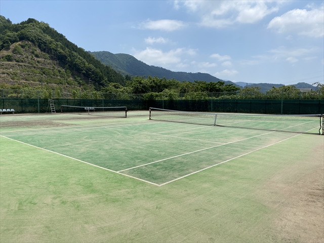 青空の下の山に囲まれた朝霧テニスコートの画像