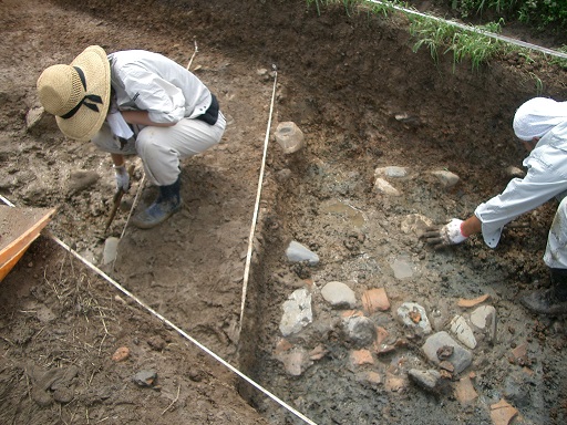 土から葺石を掘り出す作業中の2人の男性の写真