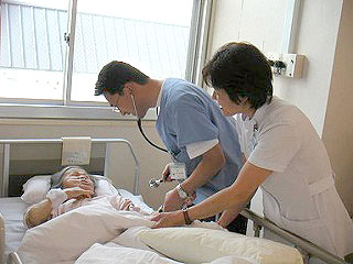 病室のベッドで寝ている女性に寄り添う医師と看護師の写真