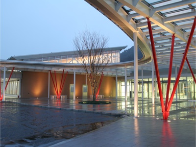 薄暗い中に建つ、赤い支柱が特徴の近代的な建物を正面から写した写真