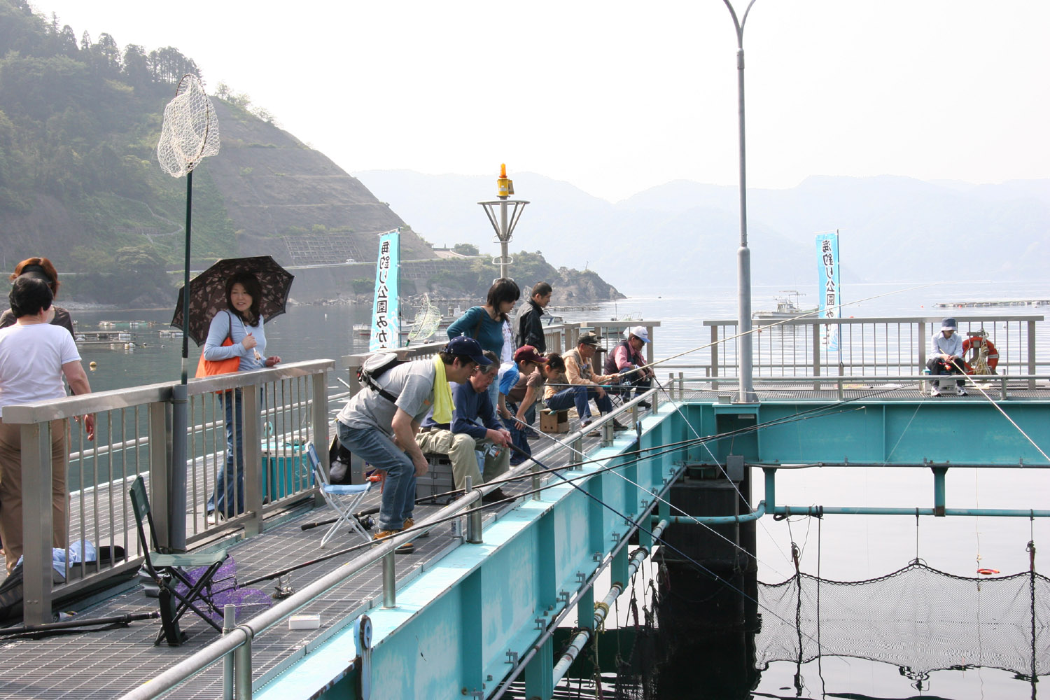 釣り橋の上に複数の人が椅子に座り釣り竿で釣りを楽しんでいる様子の写真