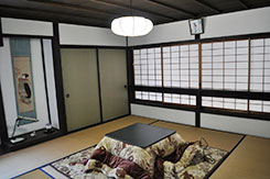 床の間に日本画がかけられ、真ん中にこたつの置かれた畳ばりの和室の写真