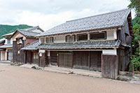 瓦は黒く、一階の外壁は木で覆われ、2階の窓は小さい古い2階建ての日本家屋の写真
