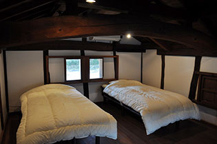 大きな太い梁の見える、白い布団のかけられたベッド二つが並ぶ部屋の写真