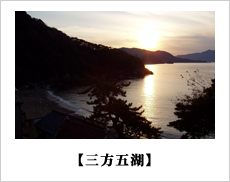 手前に湖、左側に山、山の奥に夕日が写っている風景写真