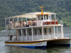 湖に浮かぶ白い2階建ての観光遊覧船で、2階に人が乗っている写真